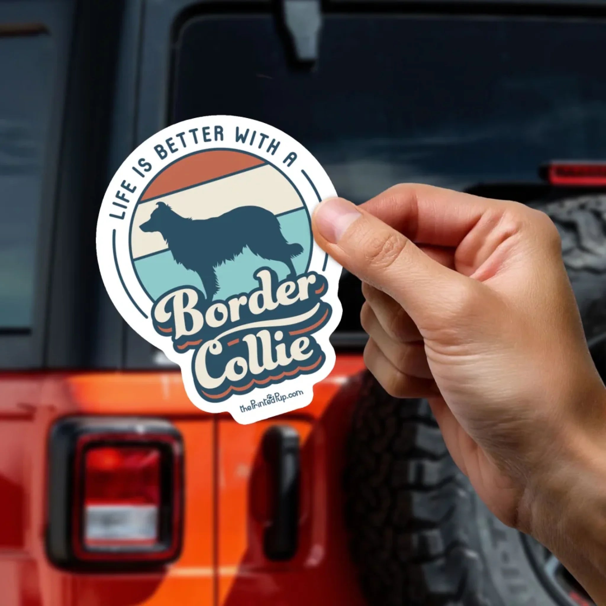 Person-Holding-Sticker_Orange-Jeep-in-Background-Mockup_Retro