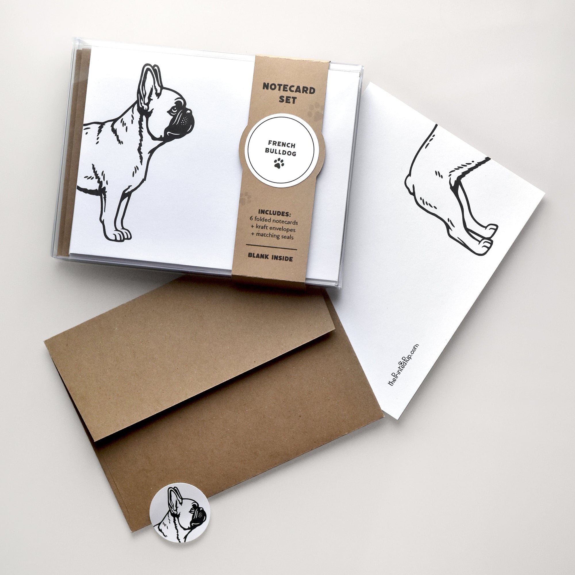 French Bulldog notecard set with clear box packaging, kraft belly band, folded card, kraft envelope, and matching round seal on a warm neutral background.